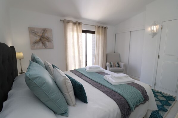 Un lit bien fait, avec des oreillers, une chaise, une lampe et une œuvre d’art représentant une étoile de mer accrochée au mur.