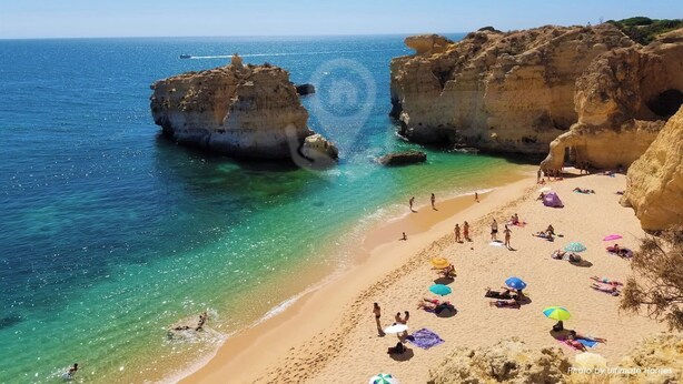 Une plage avec une eau turquoise et limpide, des falaises rocheuses et des gens qui prennent un bain de soleil.