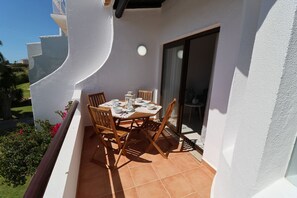 A patio with a table set for four, surrounded by wooden chairs, and a sliding glass door leading to an interior space.
