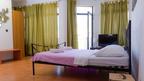 Une chambre avec un lit simple, un plancher en bois, des rideaux verts, une télévision et une table de chevet.