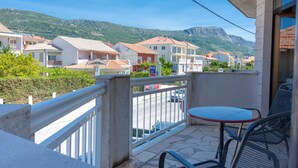 Un balcon avec une table et des chaises, donnant sur une rue bordée d’immeubles et avec une montagne en arrière-plan.