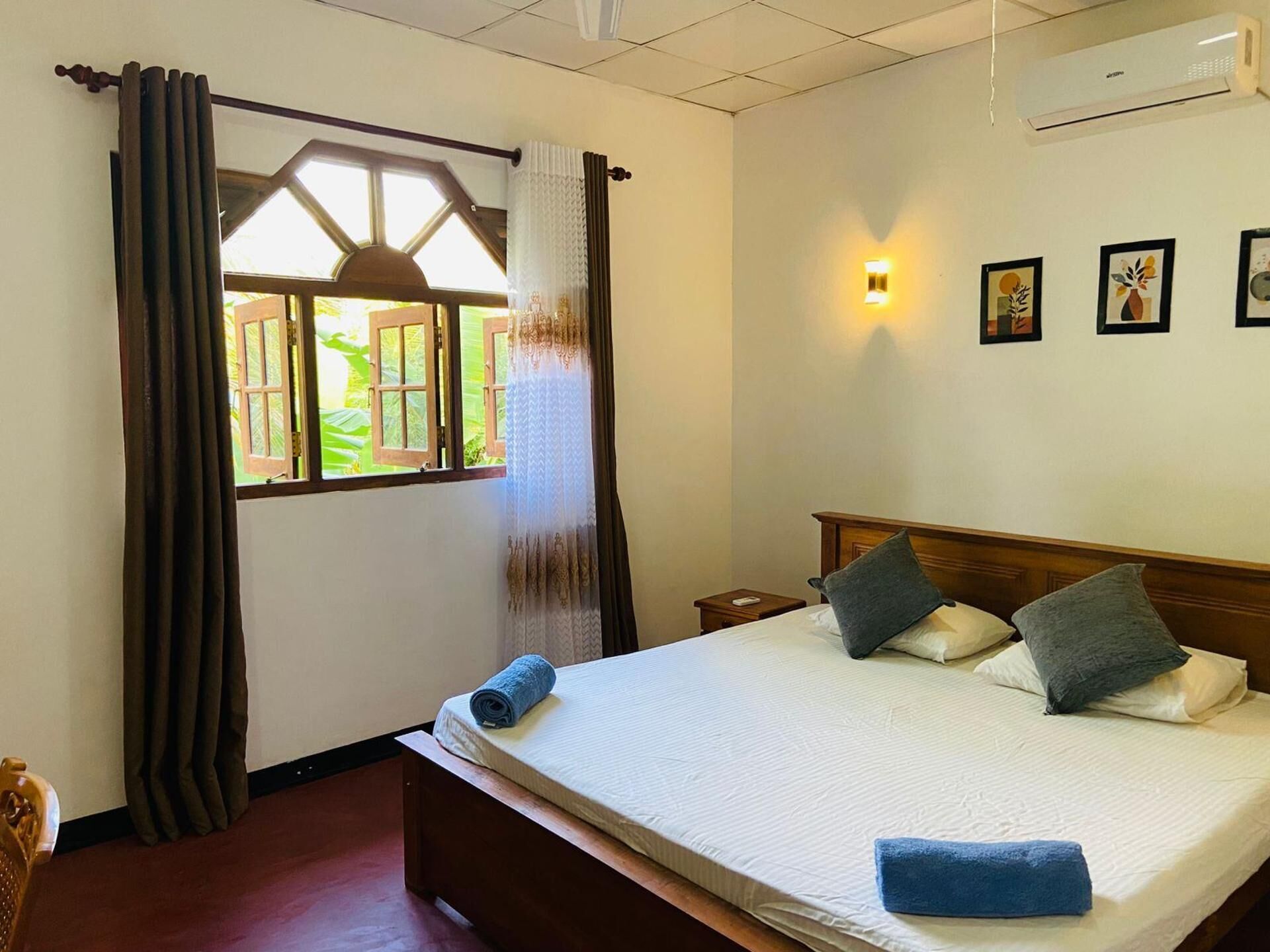 Camera d'albergo con un letto, tende, una finestra con vista aperta, un comodino e opere d'arte appese al muro.