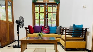 A room with a wooden sofa, a small table, a fan, and a window with a view of greenery. - Charming 2-bed Apartment in Weligama (Weligama)