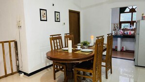 A dining area with a round wooden table, six chairs, a lit candle, and framed artwork on the wall. - Charming 2-bed Apartment in Weligama (Weligama)