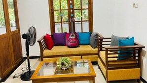 A room with a wooden sofa, a glass coffee table, a fan, and a window with decorative elements. - Charming 2-bed Apartment in Weligama (Weligama)