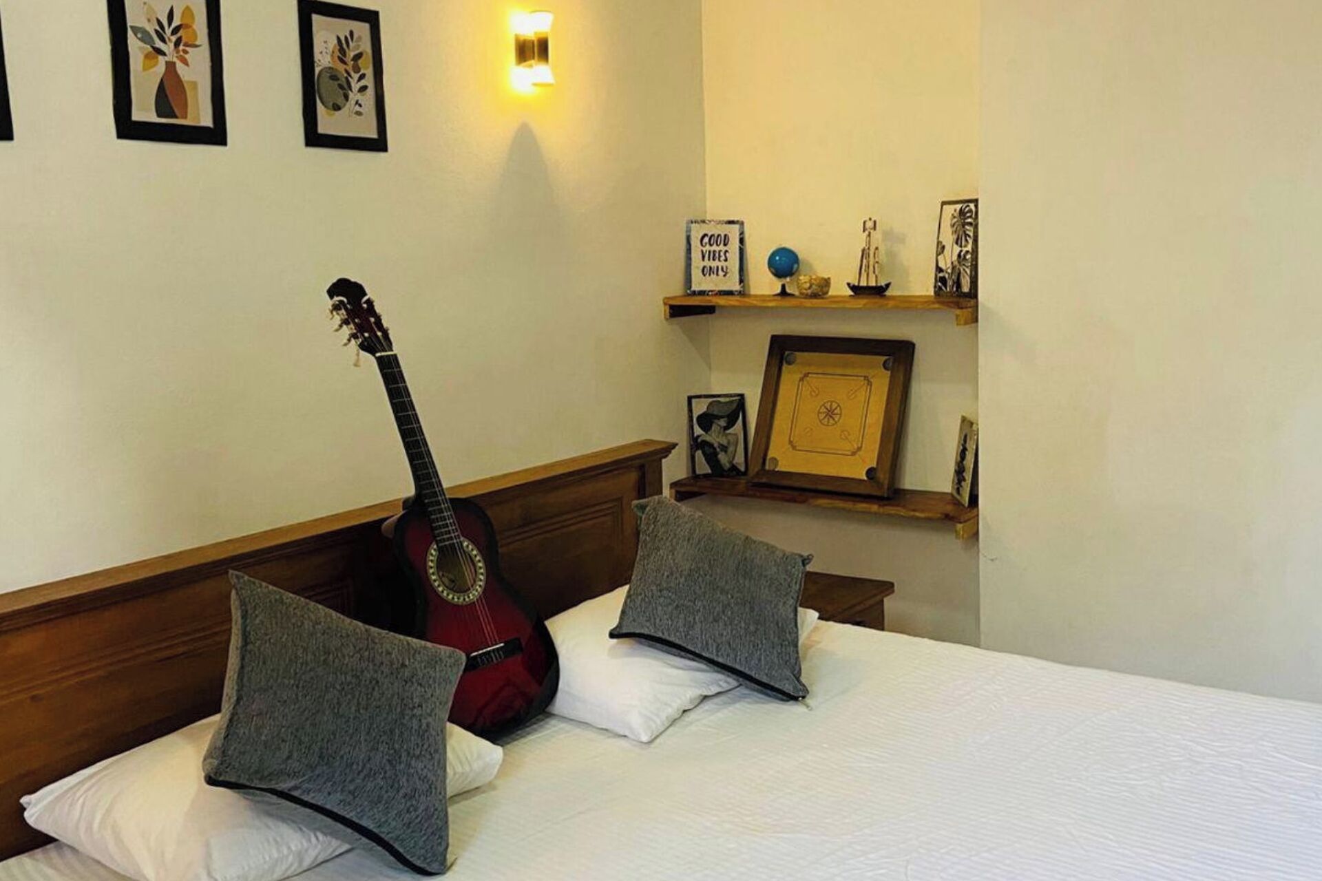 Habitación de hotel con cama, almohadas, una guitarra, decoración en la pared y una repisa con adornos.