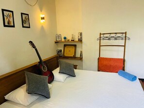 A hotel room with a bed, pillows, a guitar, a towel, a shelf with decorative items, and a wall-mounted light. - Charming 2-bed Apartment in Weligama (Weligama)