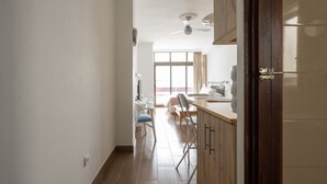 Un couloir étroit avec un ventilateur de plafond, une fenêtre avec des rideaux et un coin cuisine équipé d’un évier et d’un plan de travail.