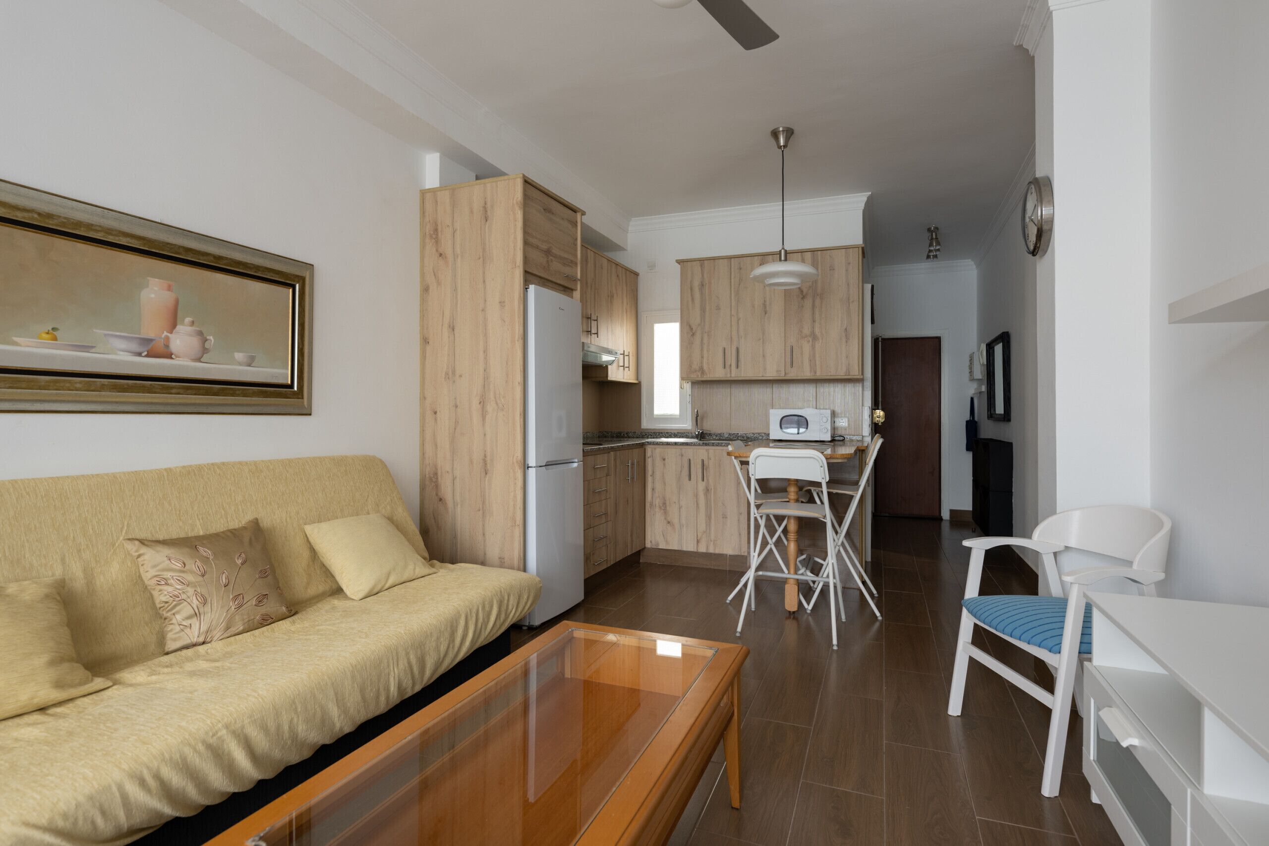A modern kitchen with wooden cabinets, a white refrigerator, and a dining area with a white chair and table.