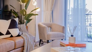 Un salon moderne avec un canapé beige, un fauteuil de couleur claire, une table basse et une grande fenêtre avec des rideaux.