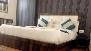 A bed with a wooden frame and white bedding, a headboard with decorative pillows, and a patterned wall in the background. - Hotel The Mars (New Delhi)