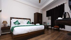 A hotel room with a wooden bed, a wardrobe, a desk with a chair, a lamp, and a coffee maker. - Hotel The Mars (New Delhi)