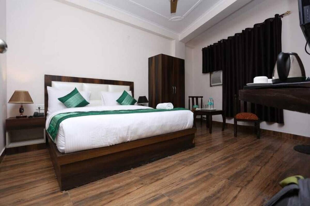 A hotel room with a wooden bed, a wardrobe, a desk with a chair, a lamp, and a coffee maker.