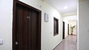 A corridor with wooden doors, a security camera, and a potted plant. - Hotel The Mars (New Delhi)