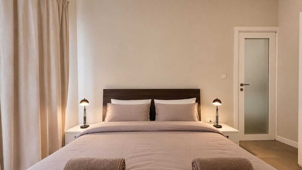 Ein Hotelzimmer mit einem Bett, zwei Nachttischlampen, einer Tür und einem Vorhang.