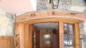 Una entrada de madera con diseños tallados, una pared de piedra y una pequeña ventana con una reja metálica.