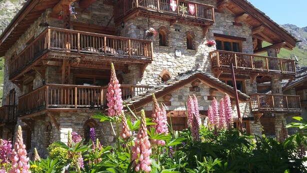 Un edificio de varios pisos de piedra con balcones de madera, rodeado de flores coloridas.