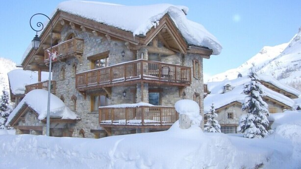 A multi-story stone building with wooden balconies, surrounded by snow-covered mountains. - N5 Chalet apartment4****South West 10/11 guests/Slopes foot (Val-d'Isère)