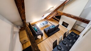 A loft-style room with exposed wooden beams, a black dining table set for four, two dark sofas, and a small white table.