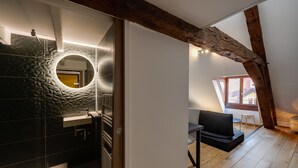 A modern bathroom with a circular mirror, black tiles, and a wooden ceiling beam.