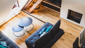 A loft-style room with a wooden floor, a black sofa, a round table, and a dining area with a black tablecloth and cutlery.