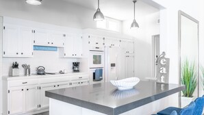 A modern kitchen with white cabinetry, a large island with a white bowl, and blue chairs.
