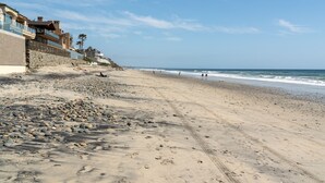 A beach with a rocky shoreline, a few people, and buildings in the background. - Ideal Location on the Sand - Beach Views and Access (Carlsbad)