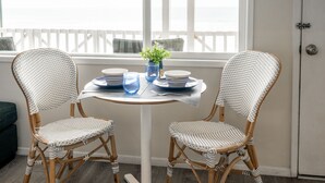 A room with two wicker chairs, a small round table, and a view of the ocean through a window. - Ideal Location on the Sand - Beach Views and Access (Carlsbad)