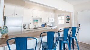 A modern kitchen with white cabinets, a wooden countertop, and blue chairs. - Ideal Location on the Sand - Beach Views and Access (Carlsbad)