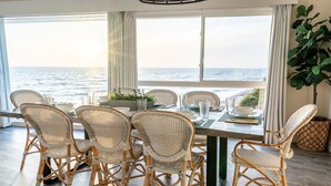 Ein Essbereich mit Korbstühlen und einem Tisch für vier Personen, mit Blick auf das Meer.