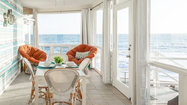 Ein Balkon mit Korbmöbeln, einem Tisch und Blick aufs Meer.