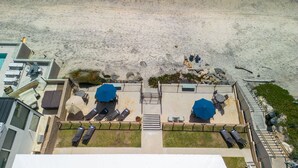 Luftaufnahme eines Hotels direkt am Strand mit Liegestühlen, Sonnenschirmen und einem Poolbereich.