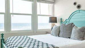 Ein Schlafzimmer mit einem Bett, gestreifte Kissen, einer gemusterten Tagesdecke, einer Lampe und Meerblick.