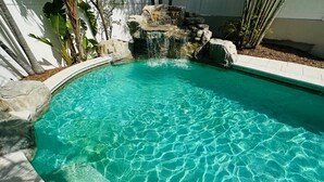 A clear blue pool with a waterfall feature, surrounded by rocks and plants.