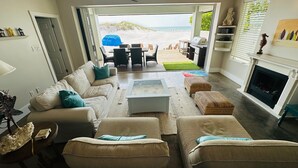A spacious living room with a view of the beach, a fireplace, and a dining area.