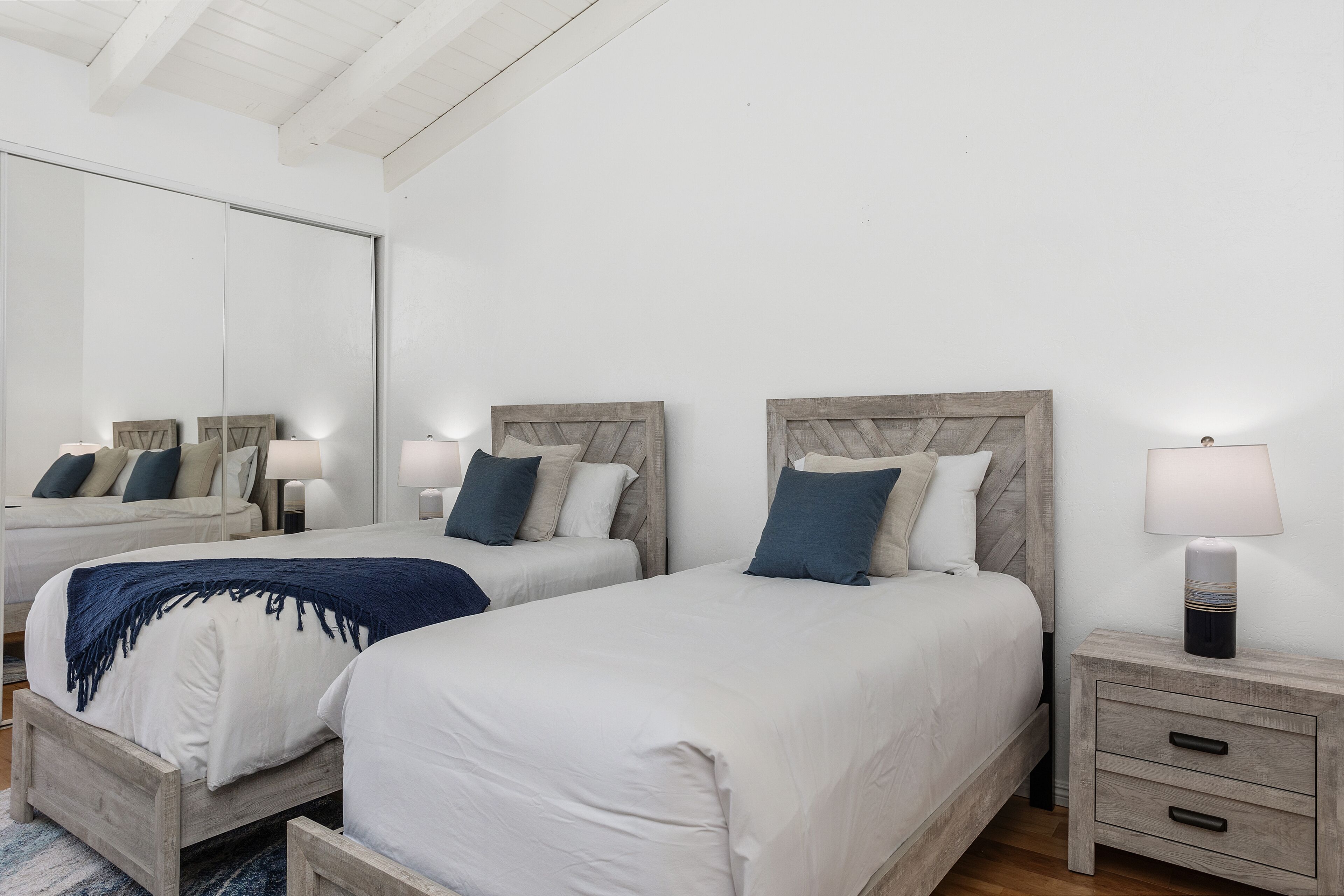 A bedroom with two beds, a nightstand with a lamp, and a large mirror.