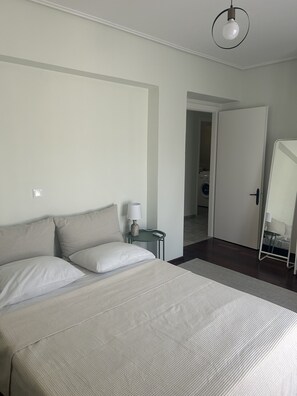 Une chambre d’hôtel comprenant un lit, une table de chevet avec une lampe, un miroir et une porte donnant sur une salle de bain.