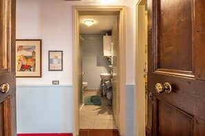 Een smalle gang die leidt naar een badkamer met een wastafel, toilet en een lijst met een kunstwerk aan de muur.