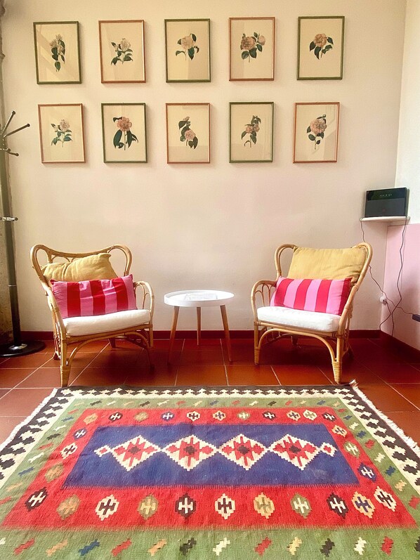 Een kamer met twee rieten stoelen met kussens, een klein rond tafeltje en een kamerkleed met dessin.