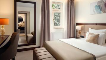 Ein Hotelzimmer mit einem großen Bett, einem Schreibtisch mit Lampe, einem Sessel, einem Spiegel und einem Fenster mit Vorhängen.