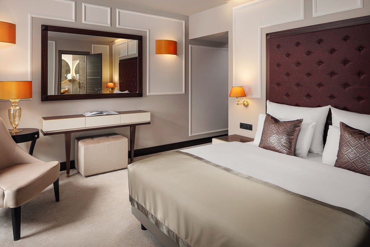 Une chambre d’hôtel équipée d’un lit, d’un bureau, d’une chaise, d’un grand miroir et d’appliques murales.