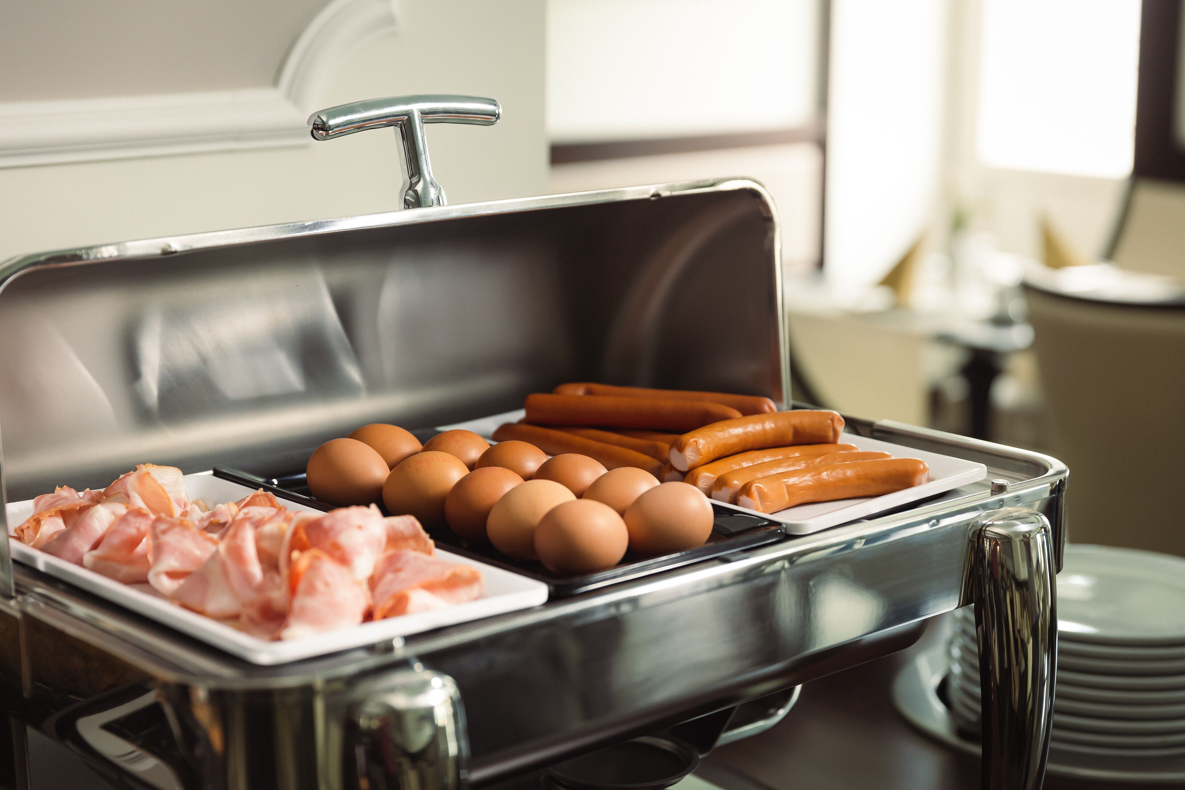 A buffet setup with various food items including eggs, sausages, and bacon.