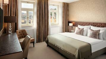 A hotel room with a bed, a desk, a chair, and a view of the city through the window.