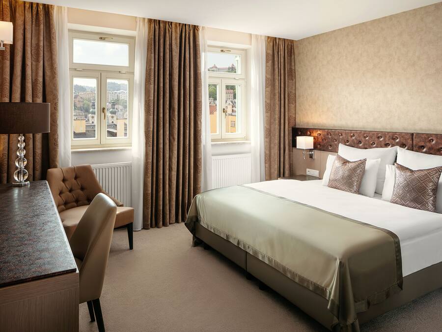 A hotel room with a bed, a desk, a chair, and a view of the city through the window.