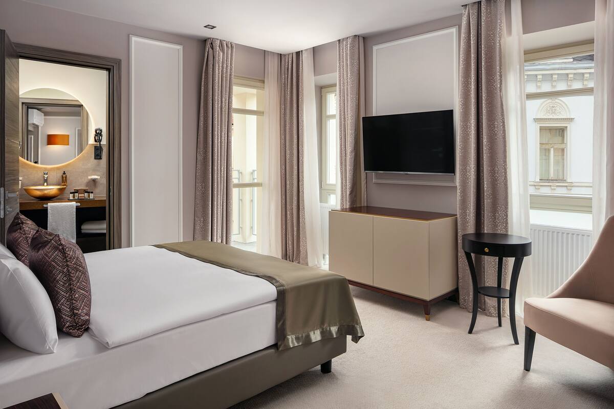 Habitación de hotel con cama, televisión, escritorio, silla y ventana con cortinas.