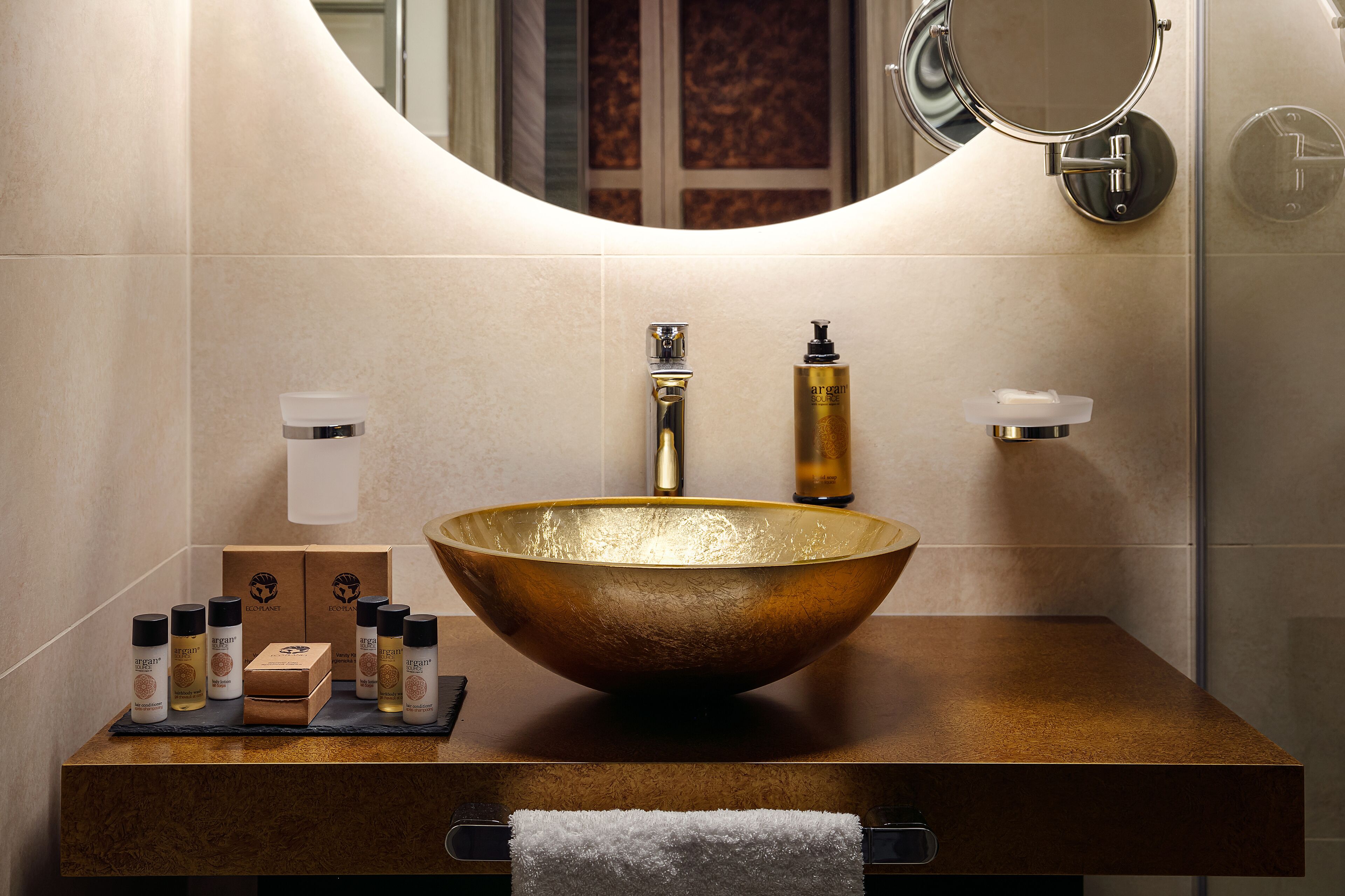 Une salle de bain avec un grand lavabo rond de couleur dorée, un miroir au-dessus et des articles de toilette posés sur le comptoir.