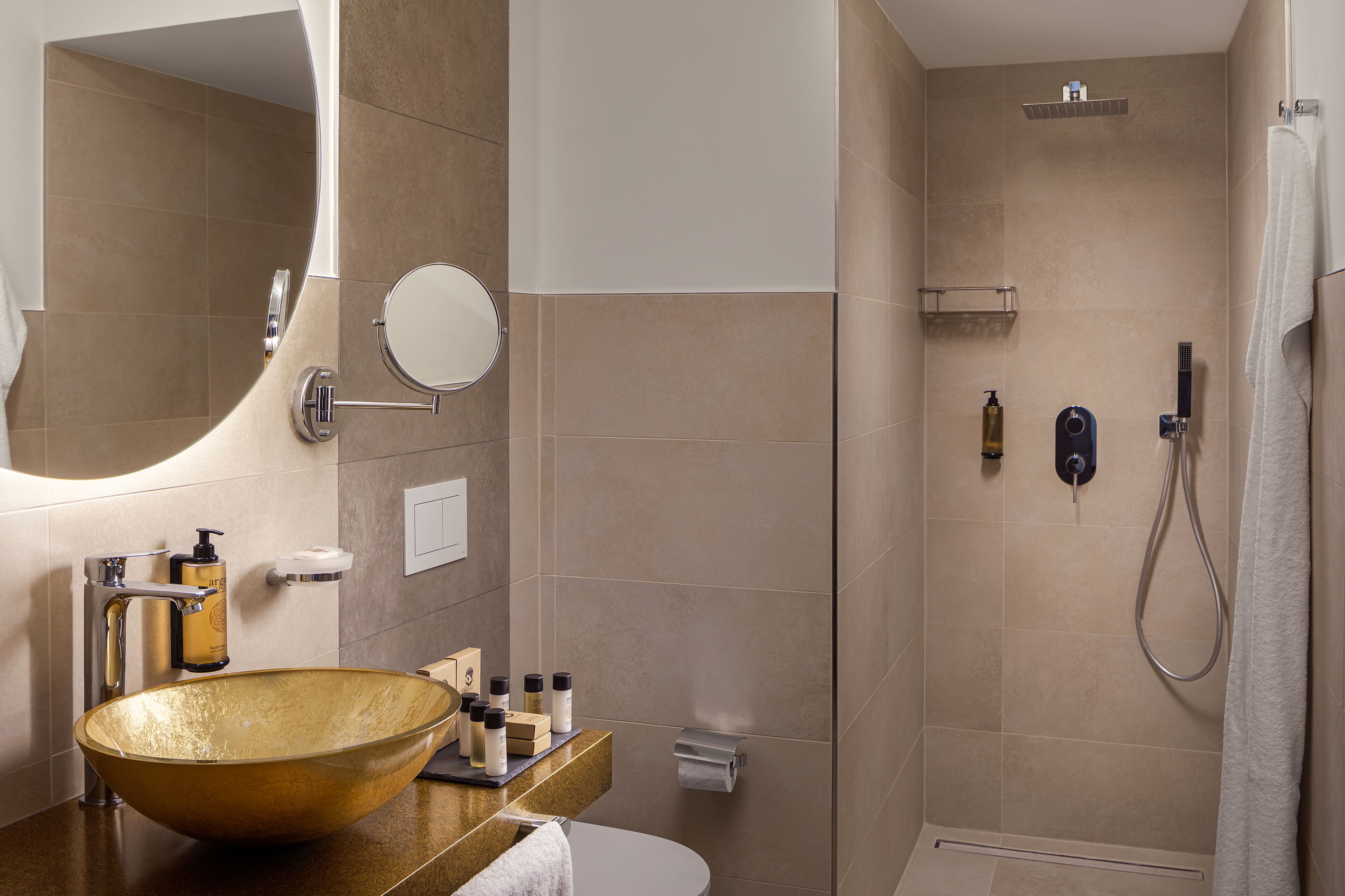 A modern bathroom with a large gold sink, a mirror, a toilet, and a shower area.