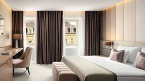 Een hotelkamer met een groot bed, een bureau, een stoel en uitzicht op gebouwen.