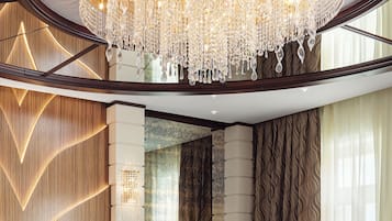 A lobby with a large chandelier, a round glass table with a vase of flowers, and a patterned rug.