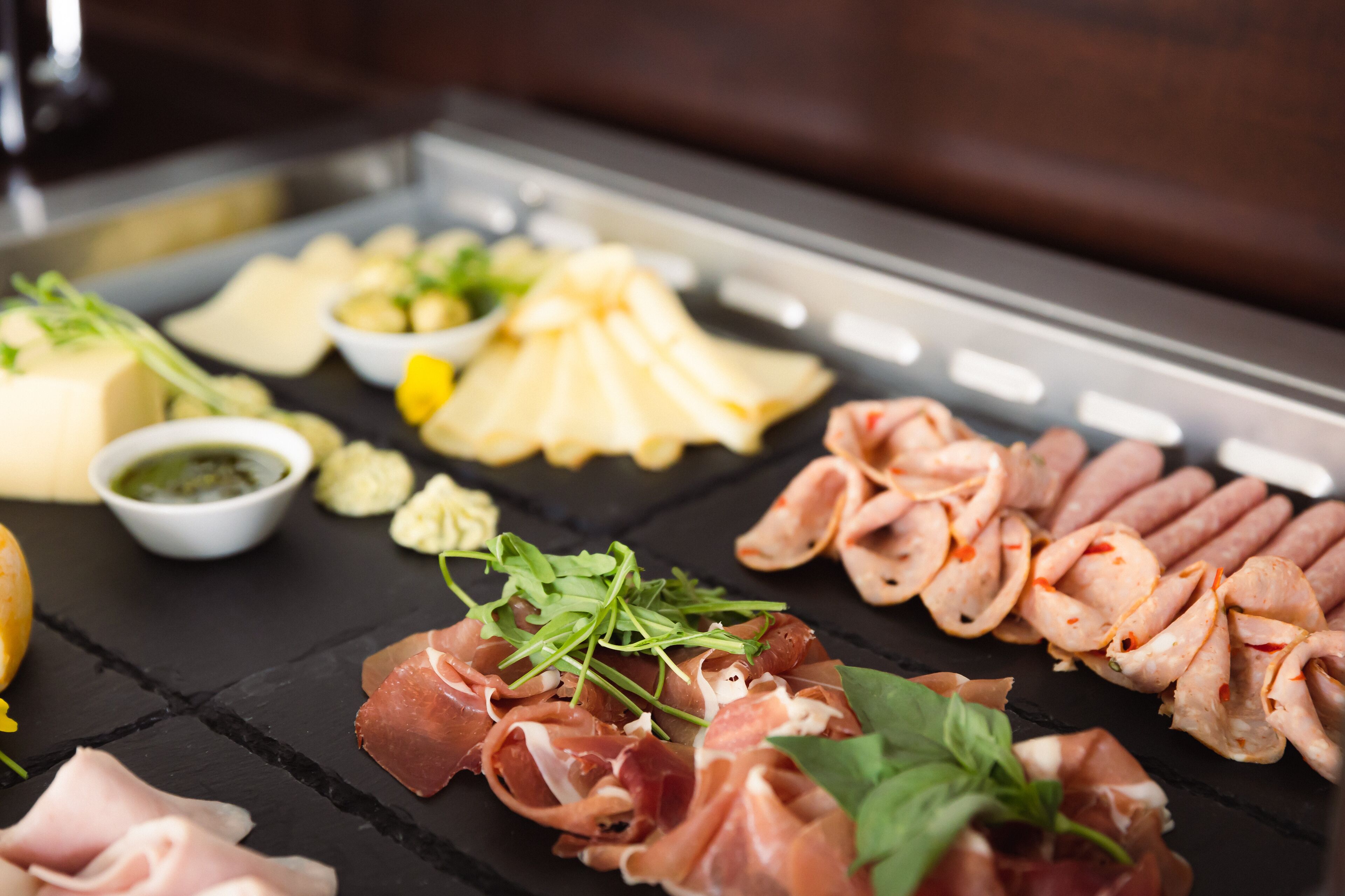 Verschiedene Speisen, darunter Fleisch, Käse und Garnituren, sind auf einer schwarzen Schieferplatte angerichtet.